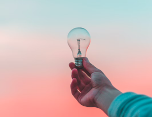 hand holding light bulb up to the sky