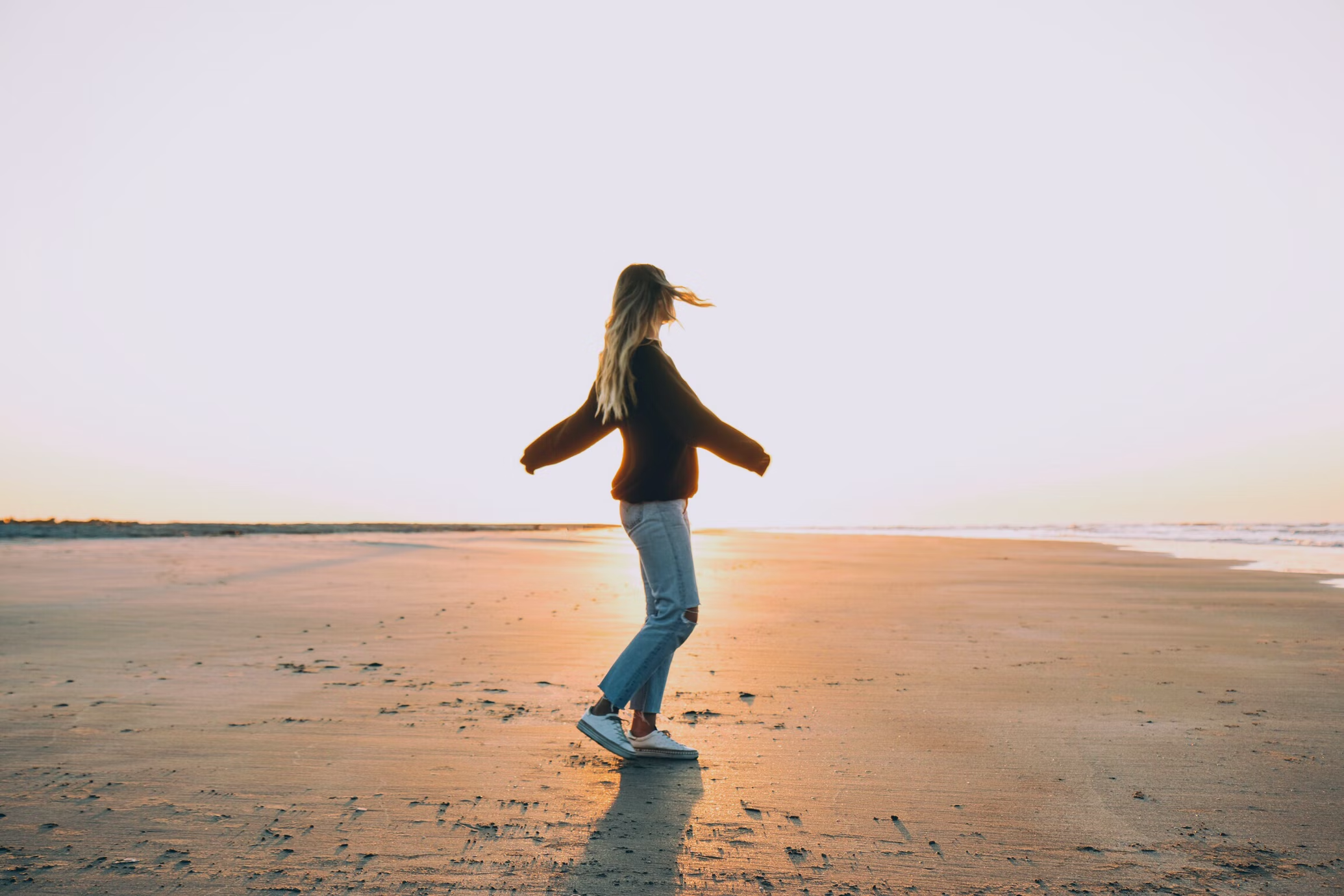 young lady in jeans and sweater standing on a beach alone and looks happy